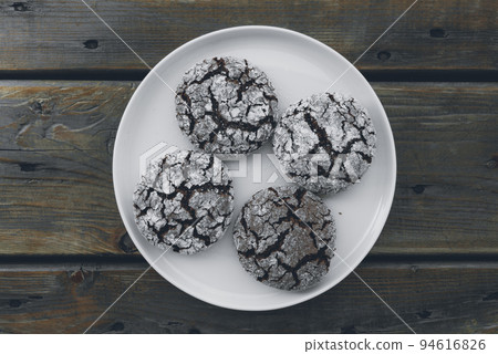 Homemade almond cookies with cocoa sprinkled with powdered sugar on a plate on a wooden background 94616826