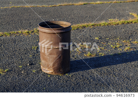 Garbage can in a metal barrel outside on asphalt at the parking lot. Garbage can in a metal barrel outside on asphalt at the parking lot. 94616973
