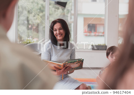 Reading time in an elementary school or kindergarten, a teacher reads a book to children in an elementary school or kindergarten. The concept of pre-school education. Selective focus 94617404