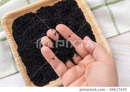 Pinch of black cumin seeds on a woman hand palm closeup. Pinch of black cumin seeds on a woman hand palm closeup. 94617445