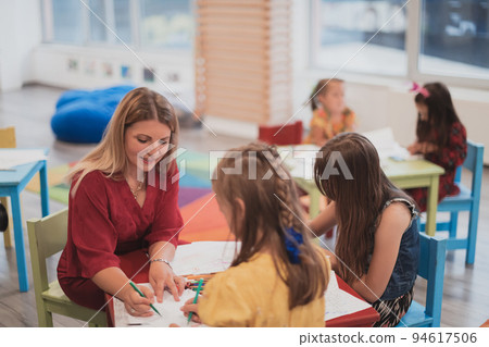 Creative kids during an art class in a daycare center or elementary school classroom drawing with female teacher.  94617506