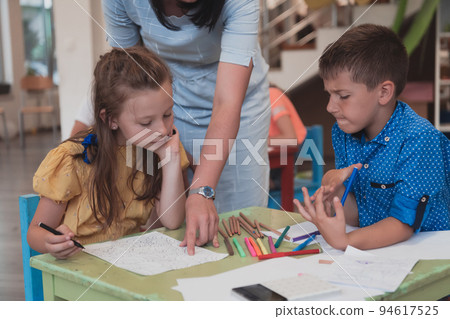 Creative kids during an art class in a daycare center or elementary school classroom drawing with female teacher.  94617525