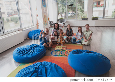 A happy female teacher sitting and playing hand games with a group of little schoolchildren A happy female teacher sitting and playing hand games with a group of little schoolchildren 94617526