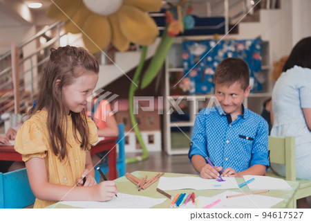 Cute girl and boy sit and draw together in preschool institution 94617527