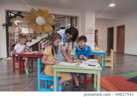 Creative kids during an art class in a daycare center or elementary school classroom drawing with female teacher.  94617541