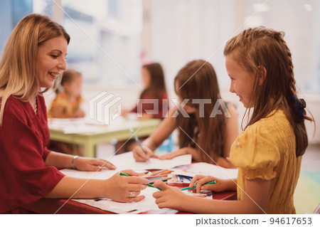 Creative kids during an art class in a daycare center or elementary school classroom drawing with female teacher. Creative kids during an art class in a daycare center or elementary school classroom drawing with female teacher. 94617653