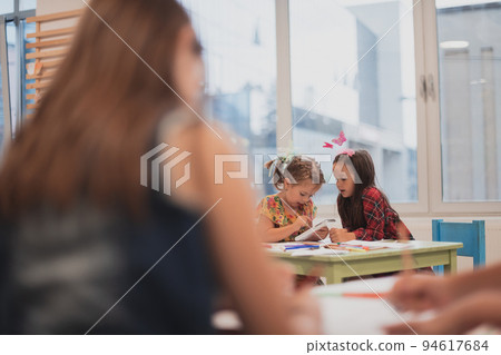 Creative kids during an art class in a daycare center or elementary school classroom drawing with female teacher. Creative kids during an art class in a daycare center or elementary school classroom drawing with female teacher. 94617684