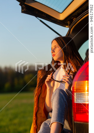 Pretty sad teenage girl with sun glasses sitting alone in a car trunk. Pretty sad teenage girl with sun glasses sitting alone in a car trunk. 94617982