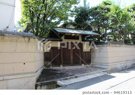 A Japanese kabuki gate with a beautiful wooden door, plastered walls, and a verdigris copper-plated roof. 94619313
