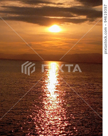 夕陽在傍晚漂浮在海面上,與雲層重疊 夕陽在傍晚漂浮在海面上,與雲層重疊 94619397