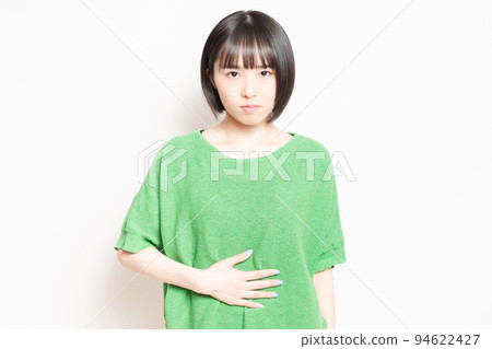 一個年輕女子在白色背景前用手摀著肚子 94622427