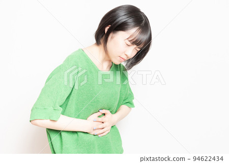 A young woman holding her stomach with her hand in front of a white background A young woman holding her stomach with her hand in front of a white background 94622434