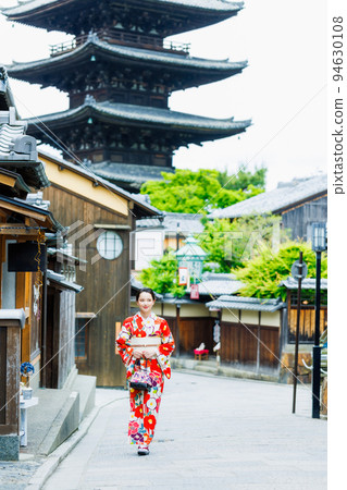 A young woman in a kimono standing with a five-storied pagoda in the background 94630108
