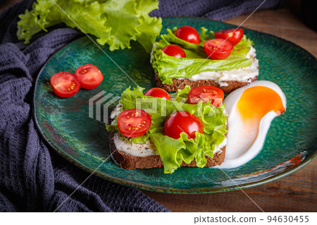 Black bread sandwich with melted cheese salad and tomatoes on a green plate. Black bread sandwich with melted cheese salad and tomatoes on a green plate. 94630455