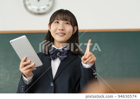 A high school girl giving a presentation with a tablet in her hand in a school classroom A high school girl giving a presentation with a tablet in her hand in a school classroom 94630574