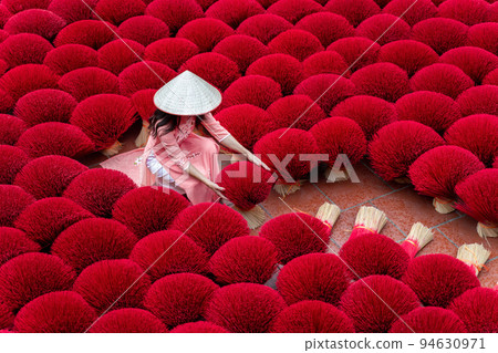 Asian woman wearing ao dai dress with Incense sticks drying outdoor in Hanoi, Vietnam. 94630971