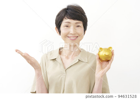 一位中年婦女拿著一個存錢罐，用她的手掌指向左邊白色背景 94631528