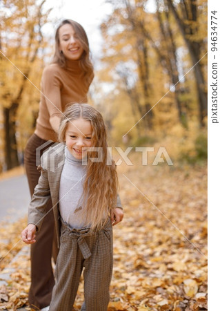 Young woman and little girl in autumn forest. Woman and her daughter playing and having fun. Girl wearing fashion grey costume with a jacket. 94634774