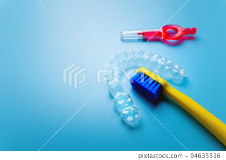 transparent plastic aligners with a yellow toothbrush and interdental brush lie on a blue background, close-up 94635516