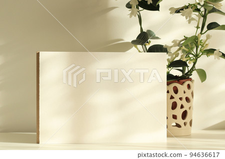 white paper sheet with jasmine plant in a pot on white table with natural shadows and sunlight white paper sheet with jasmine plant in a pot on white table with natural shadows and sunlight 94636617