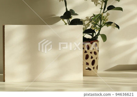 white paper sheet with jasmine plant in a pot on white table with natural shadows and sunlight white paper sheet with jasmine plant in a pot on white table with natural shadows and sunlight 94636621