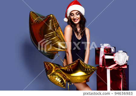 Portrait of young, sexy and beautiful woman in swimsuit and Santa hat, holding golden baloon, near gift boxes. Christmas, xmas, x-mas and winter concept 94636983