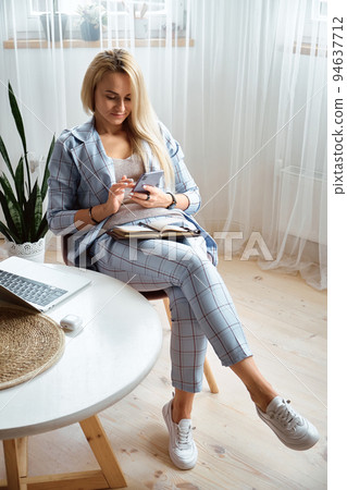 Young woman using mobile phone sitting at home office desk, remote work at home Young woman using mobile phone sitting at home office desk, remote work at home 94637712