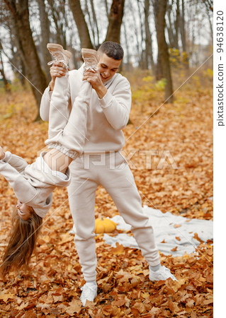Man and her little girl playing in autumn forest and laughing. Brunette man holding his daughter upside down. Family wearing beige sportive costumes. Man and her little girl playing in autumn forest and laughing. Brunette man holding his daughter upside down. Family wearing beige sportive costumes. 94638120