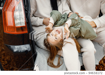 Focus on a little girl in a open car's trunk. Father, mother, their daughter hugging inside car trunk. Family wearing beige sportive costumes. 94638172