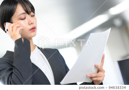 一個女人一邊看材料一邊打電話 94638334