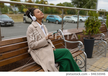 young african american woman in an autumn coat listens to music with enjoyment closing her eyes young african american woman in an autumn coat listens to music with enjoyment closing her eyes 94638946