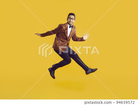 Cheerful funny dark-skinned young man in leopard jacket having fun jumping on yellow background. 94639572