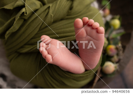 The tiny foot of a newborn. Soft feet of a newborn in a green woolen blanket. Close up of toes, heels and feet of a newborn baby. Studio Macro photography. Woman's happiness. The tiny foot of a newborn. Soft feet of a newborn in a green woolen blanket. Close up of toes, heels and feet of a newborn baby. Studio Macro photography. Woman's happiness. 94640656