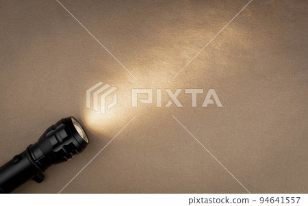 A bright beam of light from a flashlight shines on a brown recycled craft paper background. Old grunge vintage highly textured paper background 94641557