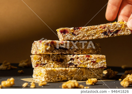 Woman takes Homemade Granola energy bar. Variety of protein granola breakfast bars, with nuts, raisins dried cherries and chocolate. Healthy nutrition eating Gluten free cereal dieting snack super 94641826