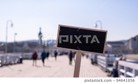 Blank Black billboard against Crowds of tourists The Sopot Pier in the city on the Baltic Sea. Empty mockup template Visitors walking The pier is the longest wooden pier in Europe. Blackboard label 94641856