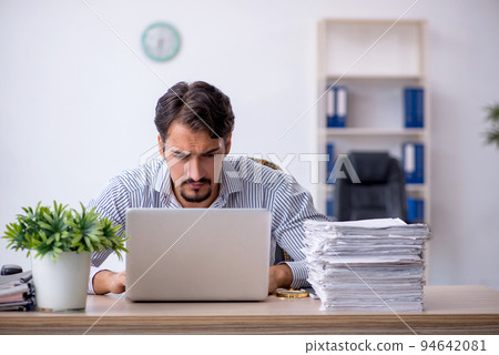 Young male employee unhappy with excessive work in the office Young male employee unhappy with excessive work in the office 94642081