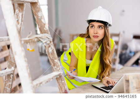 Woman worker checking documents and using laptop in construction site Woman worker checking documents and using laptop in construction site 94645165