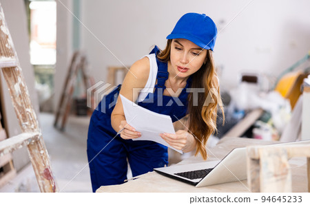 Female contractor in blue uniform using laptop at construction site 94645233