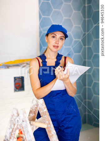 Focused woman dressed in work clothes checking quantity of tiles in documents during repair works Focused woman dressed in work clothes checking quantity of tiles in documents during repair works 94645330