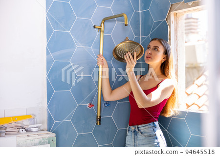 Beautiful woman chooses place to install new shower during renovation work in bathroom 94645518
