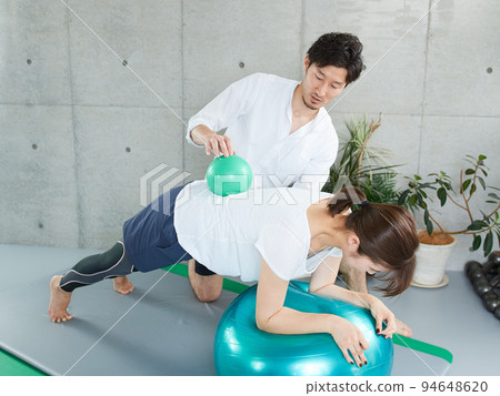 Japanese woman receiving plank instruction from a personal trainer 94648620