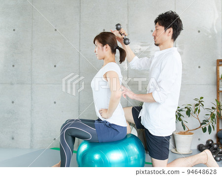 Japanese woman receiving dumbbell training guidance from a personal trainer 94648628