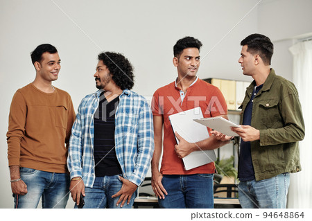 Cheerful start-uppers standing in office, smiling and looking at each other Cheerful start-uppers standing in office, smiling and looking at each other 94648864