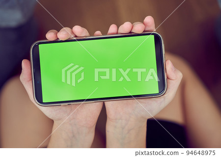 Close-up of children's hands using a phone with a green screen. A little girl is sitting on the floor and holding a smartphone with a colored key. High quality photo 94648975