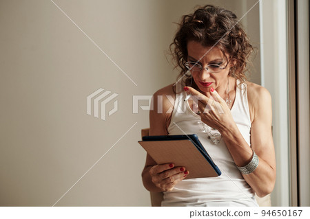 Shocked glam rock mature woman smoking when reading news article on tablet computer Shocked glam rock mature woman smoking when reading news article on tablet computer 94650167