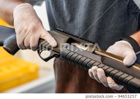 Close up of young man in apron disassembling a gun above the table 94653257