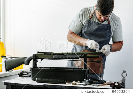 Close up of a man in apron wiping his firearm with a cloth Close up of a man in apron wiping his firearm with a cloth 94653264