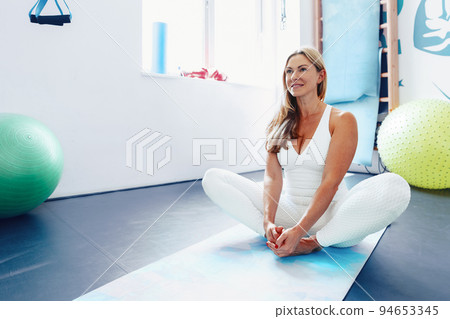 Middle-aged woman stretching on exercise mat at a gym. Middle-aged woman stretching on exercise mat at a gym. 94653345