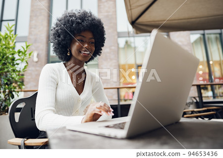 Smiling young african woman sitting with laptop in coffee shop 94653436